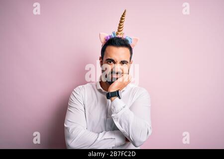 Young handsome man with beard wearing funny unicorn diadem over pink background thinking looking tired and bored with depression problems with crossed Stock Photo