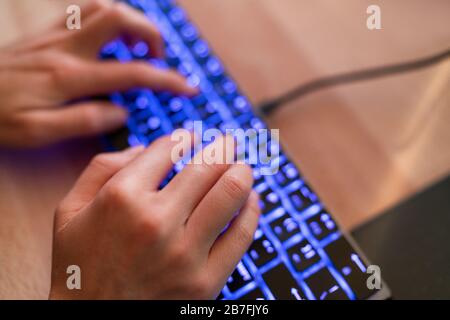Gamer pc computer keyboard woman typing on blue backlit gaming key board working late at night on home office desk. Stock Photo
