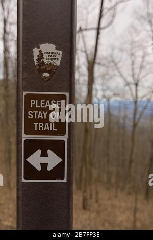 A trail marker in Cumberland Gap National Historic Park telling hikers to stay on the trail with arrows showing where it is. Background is blurred out Stock Photo
