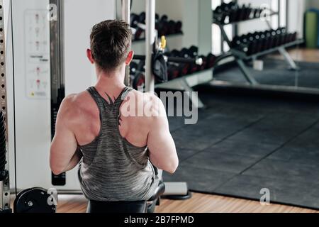 Fit strong man doing exercise on rowing machine in sports center, view from the back Stock Photo