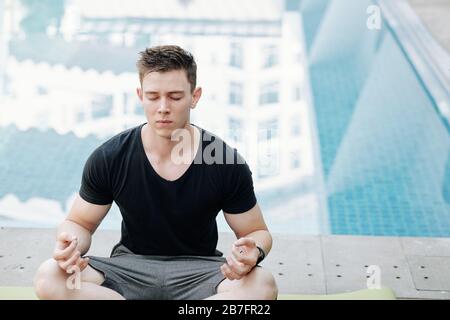 Handsome young man meditating in lotus position with his eyes closed Stock Photo