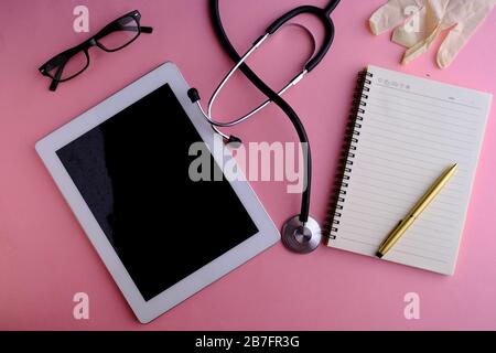 top view of digital tablet, pills and stethoscope on pink background. Stock Photo