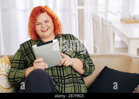 Portrait of pretty young plus size woman laughing when watching comedy movie on tablet computer Stock Photo