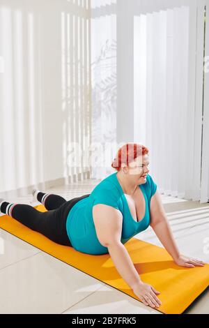 Overweight young woman in sports clothes practicing yoga at home Stock Photo