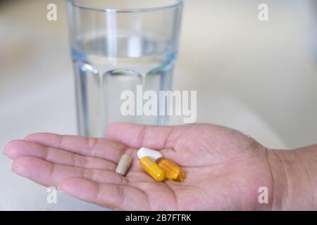 A woman with a selection of natural health supplements in the palm of her hand ready to take with a glass of water