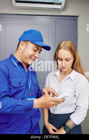 Technician in uniform explaining young woman how to use air conditioner remote control Stock Photo