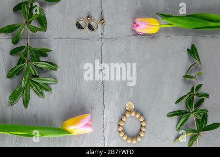 Jewelry, bracelet with keychain and gold earrings together with tulips and green laid on a concrete background. Inside the composition, free space Stock Photo