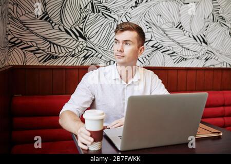 Portrait of pensive handsome young man drinking coffee when working in cafe Stock Photo