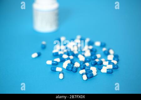 Double colored blue and white capsuls pills tablets isolated on blue background, behind white pharmaceutical bottle in soft focus Stock Photo