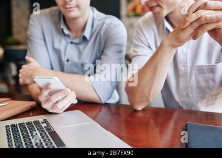 Young businessman showing text message or mobile application on smartphone screen to colleague at meeting Stock Photo