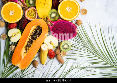 Summer composition from different sliced exotic fruits and tropical leaves. Fresh sliced apple, mango, orange, kiwi, papaya, maracuja, dragon fruit, r Stock Photo