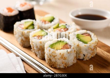 Close up on a serving of uramaki sushi rolls with fresh avocado pear and salmon in nori and rice rolled in sesame seeds on a wooden tray at the table Stock Photo