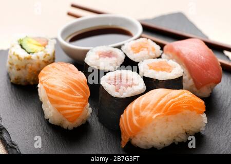 Selection of different sushi served at a meal on a black wooden tray with salmon nighiri sushi and uramaki rolls served with soy sauce dip and chopsti