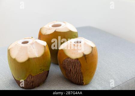 Three green coconuts with holes for straw stand on a gray sofa surface Stock Photo