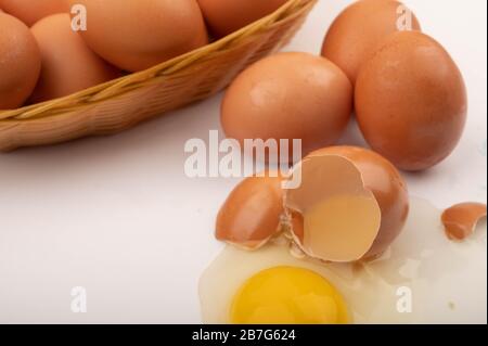 A broken chicken egg, chicken eggs in a wicker basket and eggs scattered on a white background. Close up Stock Photo