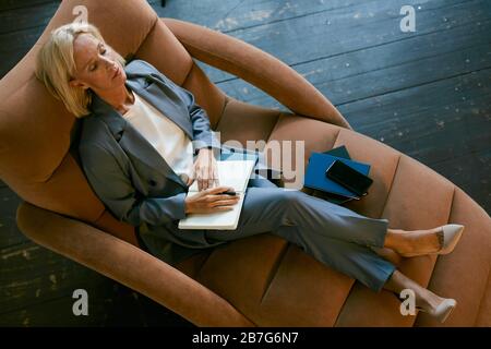 Above view portrait of stressed mature businesswoman relaxing in lounge chair lying with eyes closed, copy space Stock Photo