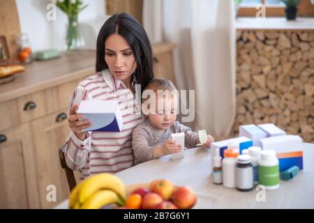 Young mom reading medicine instruction, holding her daughter Stock Photo