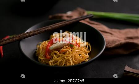 Cropped shot of Schezwan Noodles or Chow Mein in black bowl with chopsticks  on black table Stock Photo