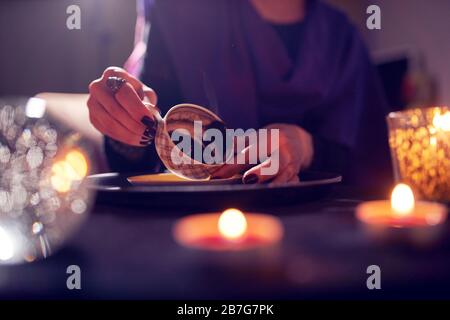 Fortune teller divines on coffee grounds at table with ball of predictions in room Stock Photo