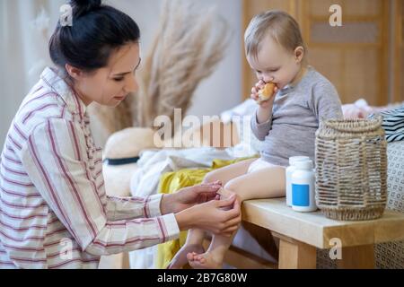 Young mom applying plaster on daughter's knee Stock Photo