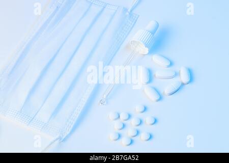 electronic thermometer, protective mask, pipette and tablets pills lie on a white background with blue illumination Stock Photo