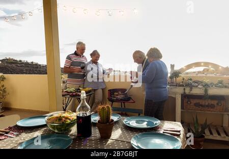 Senior happy couples eating and drinking wine at barbecue dinner outdoor - Mature people having fun dining and laughing together - Main focus on left Stock Photo