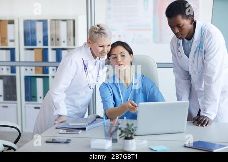 Multi-ethnic group of doctors using laptop while working on medical project together, copy space Stock Photo