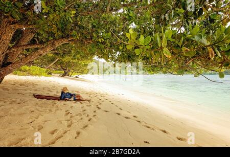 Handsome man lying on the beach and reading book. Summer time. Tourist relaxing on a tropical beach Stock Photo