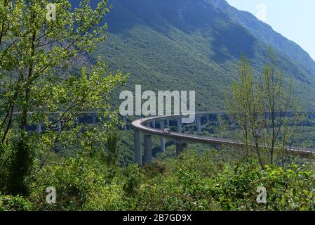 A delivery truck driving an elevated motorway in North Italy. The motorway is sunrounded by mountains and vegetation. Stock Photo