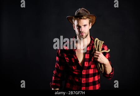 Lassoing on prairie. Lasso tool of American cowboy. Still used on ranches to capture cattle or other livestock. Western life. Man unshaven cowboy black background. Cowboy wearing hat hold rope. Stock Photo