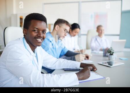 Portrait of young African-American doctor smiling at camera during medical council or conference in clinic, copy space Stock Photo