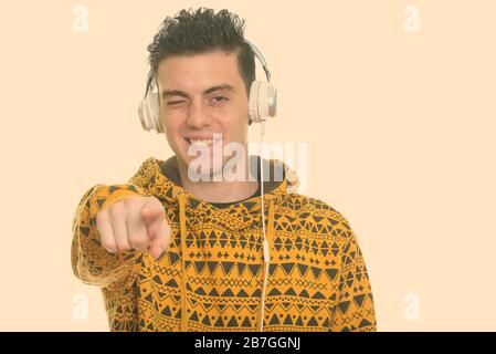 Happy young man smiling and winking while listening to music and pointing finger at camera Stock Photo
