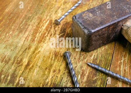 Old rusty hammer and three steel nails lie on a scratched wooden table. Copy space for text. Selective focus. Home work concept. Close-up. Stock Photo