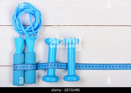 Centimeter tied around sports equipment in cyan blue on wooden vintage  background. Tools for healthy lifestyle. Workout and weight loss concept.  Bottle, apple, measuring tape and jump rope, top view Stock Photo 