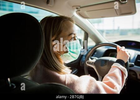 Woman in protective mask driving a car on road. Safe traveling. Stock Photo