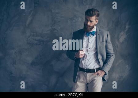 Portrait of young bearded guy in a suit stands on a gray background and looks inquiringly Stock Photo