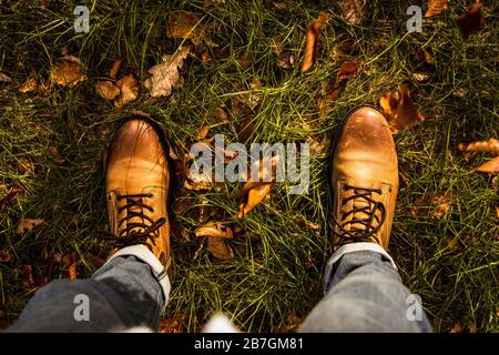 Autumn fibes top down of leather boots and rolled up trousers surrounded by grass and leaves that fell out of trees, outdoors