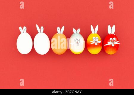 White, brown and colorful painted easter eggs with funny bunny ears and cartoon faces on red background Stock Photo