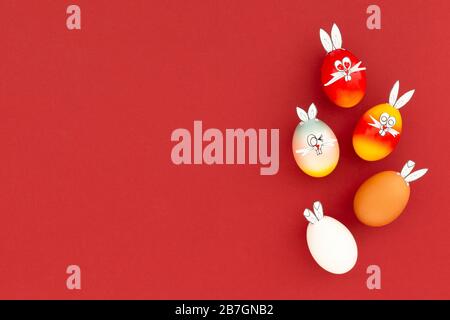 White, brown and colorful painted easter eggs with funny bunny ears and cartoon faces on red background Stock Photo