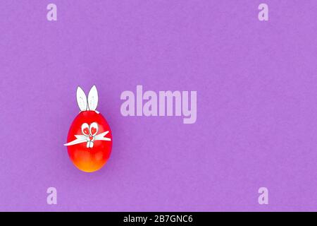 Colorful painted easter egg with funny bunny ears and cartoon face on purple background Stock Photo