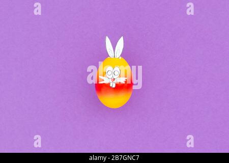 Colorful painted easter egg with funny bunny ears and cartoon face on purple background Stock Photo
