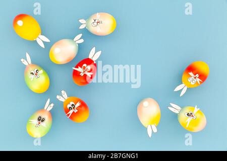 Colorful painted easter eggs with funny bunny ears and cartoon faces on light blue background Stock Photo
