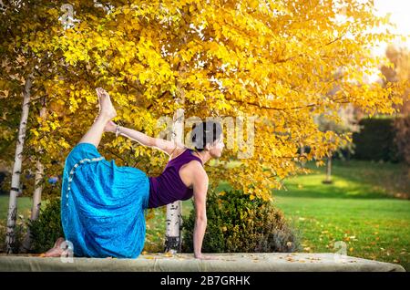 Young woman doing yoga in autumn city park near yellow birch trees Stock Photo