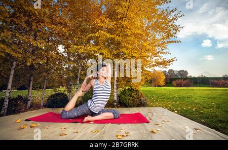 Young woman doing yoga in autumn city park near yellow birch trees Stock Photo