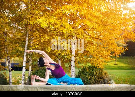 Young woman doing yoga in autumn city park near yellow birch trees Stock Photo