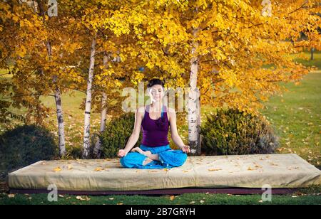 Young woman doing yoga in autumn city park near yellow birch trees Stock Photo