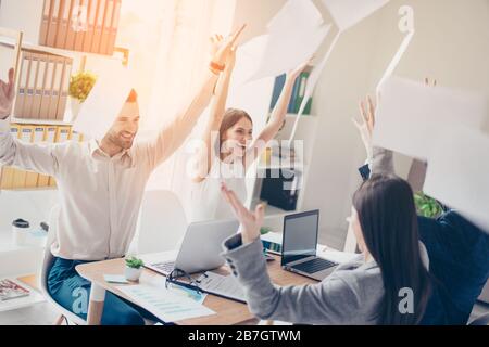 Victory! Cheerful successful businesspartners celebrating breakthrough in their modern sunny workplace throwing documents up Stock Photo