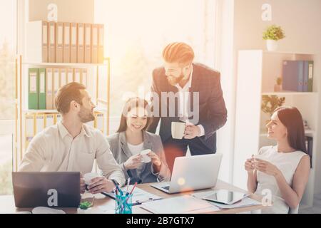Cheerful happy colleagues in smart clothes having nice conversation during the break in office smiling and drinking coffee Stock Photo