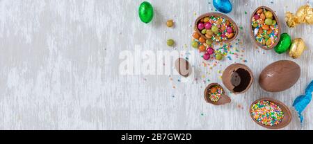 Chocolate easter eggs with sprinkles and other candy on white wooden table top - flat lay banner holidays and celebrations concept image with copy spa Stock Photo