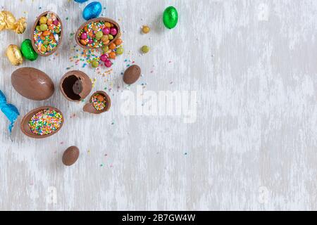 Chocolate easter eggs with sprinkles and other candy on white wooden table top - easter holiday concept image with copy space fort text. Stock Photo